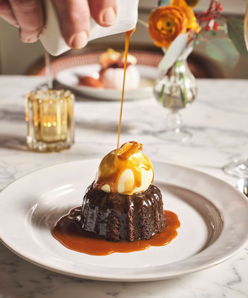 Sticky toffee pudding. Drizzling caramel sauce onto a sticky toffee pudding, topped with vanilla ice cream.